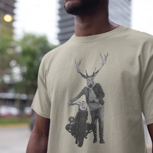May include: Beige t-shirt featuring a black and white illustration of a deer-headed figure leaning on a vintage motorcycle. The figure is wearing a jacket, jeans, and boots. The motorcycle has a round headlight and a classic design.