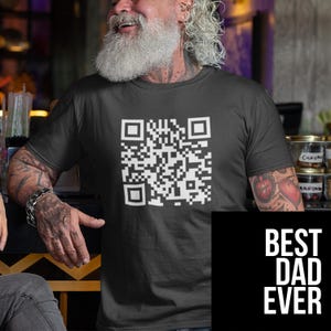 May include: Black t-shirt with a large white QR code graphic on the front. The lower right corner features a black square with the white text "BEST DAD EVER". The shirt is short-sleeved.