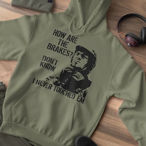 May include: A green hooded sweatshirt with a black graphic print of a man in a racing helmet. The text on the graphic reads "How are the brakes? Don't know. I never touched em."