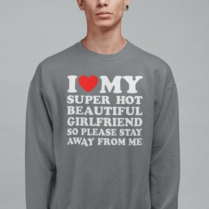 May include: Gray sweatshirt with white text that reads "I &hearts; MY SUPER HOT BEAUTIFUL GIRLFRIEND SO PLEASE STAY AWAY FROM ME". A red heart is in place of the word "love".