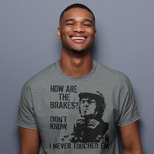 May include: A heather grey t-shirt featuring a black and white image of a man wearing a helmet and the text "How are the brakes? Don't know. I never touched 'em."