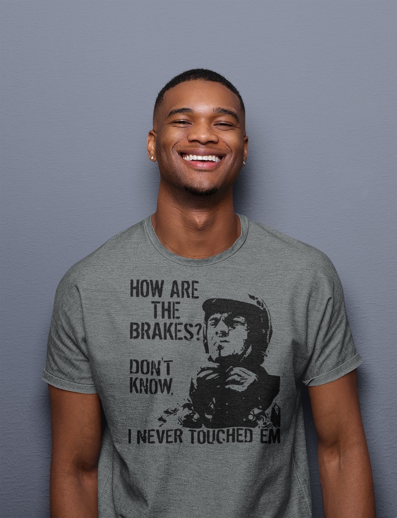 May include: A heather grey t-shirt featuring a black and white image of a man wearing a helmet and the text "How are the brakes? Don't know. I never touched 'em."