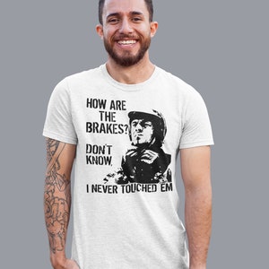 May include: A white t-shirt with a black and white graphic print of a man in a racing helmet. The text on the shirt reads "How are the brakes? Don't know. I never touched 'em."