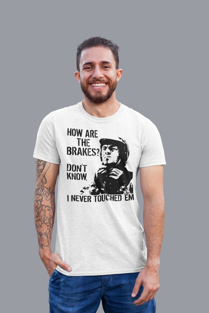 May include: A white t-shirt with a black and white graphic print of a man in a racing helmet. The text on the shirt reads "How are the brakes? Don't know. I never touched 'em."