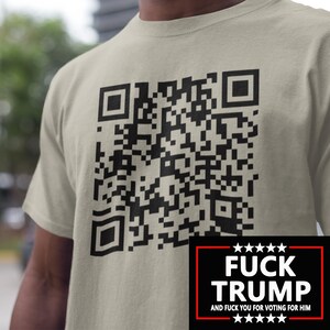 May include: A light tan t-shirt featuring a large black QR code. Beneath the code is a black rectangle with the white text "FUCK TRUMP" and the words "AND FUCK YOU FOR VOTING FOR HIM".