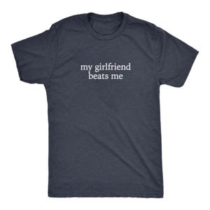 May include: A navy blue t-shirt with the white text "my girlfriend beats me" printed across the chest. The shirt has short sleeves and a crew neck. The fabric appears to be a soft, heathered material.