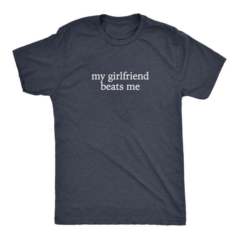 May include: A navy blue t-shirt with the white text "my girlfriend beats me" printed across the chest. The shirt has short sleeves and a crew neck. The fabric appears to be a soft, heathered material.