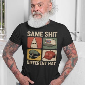 May include: Black t-shirt with the text "SAME SHIT DIFFERENT HAT" and four images of different hats. The hats include a white hood, a hat with a Confederate flag, a military hat, and a red "Make America Great Again" hat.