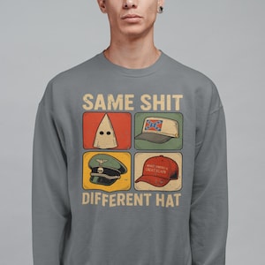 May include: Gray sweatshirt with the text "SAME SHIT DIFFERENT HAT" and four images of hats: a KKK hood, a Confederate flag hat, a military cap, and a "Make America Great Again" hat.