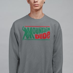 Może przedstawiać: Szara bluza z zielonym i czerwonym nadrukiem graficznym z napisem "Mountain Dude". Grafika zawiera r&oacute;wnież sylwetkę osoby.