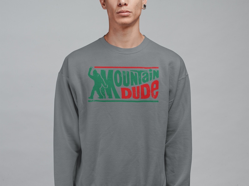 Może przedstawiać: Szara bluza z zielonym i czerwonym nadrukiem graficznym z napisem "Mountain Dude". Grafika zawiera r&oacute;wnież sylwetkę osoby.