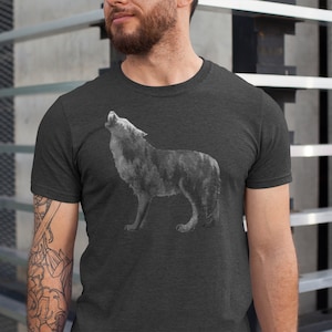 May include: A dark heather grey t-shirt with a wolf howling at the moon graphic. The wolf is made up of a forest scene.