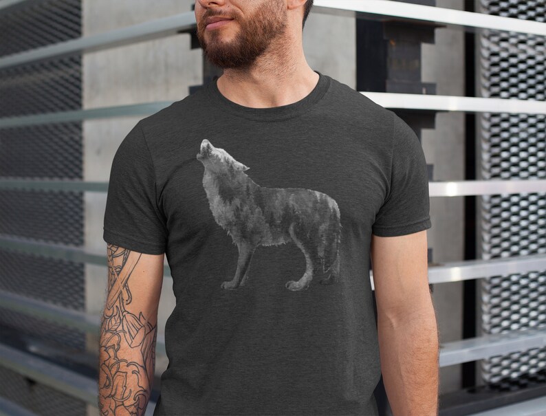 May include: A dark heather grey t-shirt with a wolf howling at the moon graphic. The wolf is made up of a forest scene.