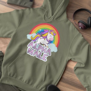 May include: Olive green hoodie with a front pocket, a drawstring hood, and a graphic of a unicorn with a rainbow and the text "ALPHA MALE". The image also shows a matching beanie, pants, and black sneakers.