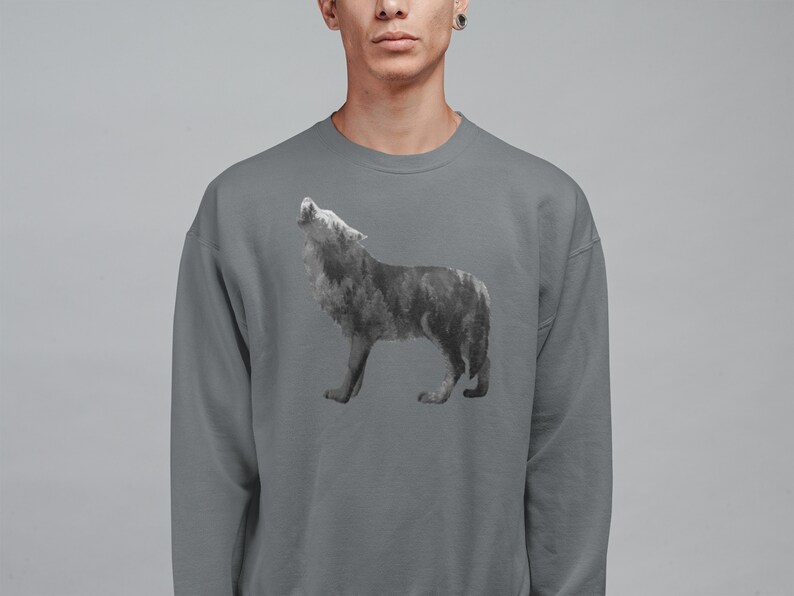 May include: A gray sweatshirt with a wolf silhouette design. The wolf is made up of a forest scene, with trees and foliage forming its shape.