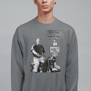 May include: A gray sweatshirt with a black and white image of a man riding a motorcycle. The image is in front of a sign that reads "ACHTUNG 100 m Schweizer Grenze 607 HALT".