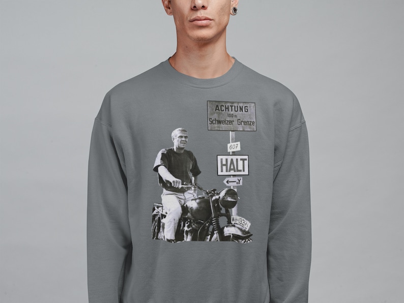 May include: A gray sweatshirt with a black and white image of a man riding a motorcycle. The image is in front of a sign that reads "ACHTUNG 100 m Schweizer Grenze 607 HALT".