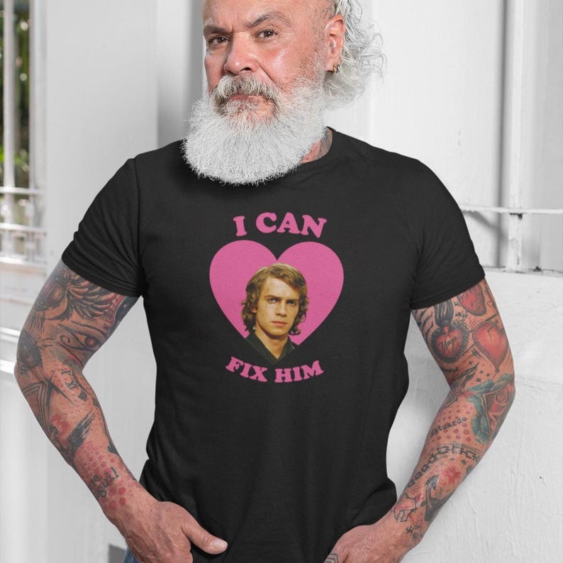 May include: Black t-shirt with a pink heart graphic featuring a portrait and the text "I CAN FIX HIM". The shirt is made of a soft material and is suitable for casual wear.