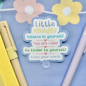May include: A blue sticker with the text "Little reminders" and four positive affirmations: "Believe in yourself", "You are valid", "Be kinder to yourself", and "Know your worth".