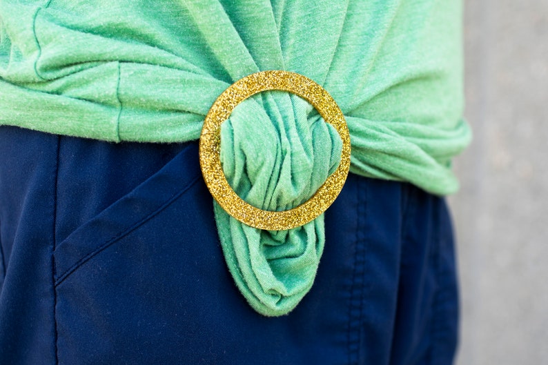 May include: A green shirt tied at the waist with a gold glitter belt.