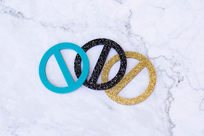 May include: Three round, decorative, paper cutouts with a line through the center. The cutouts are turquoise, black with glitter, and gold with glitter.