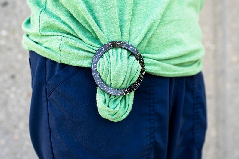 May include: A green shirt tied at the waist with a black and white speckled ring.