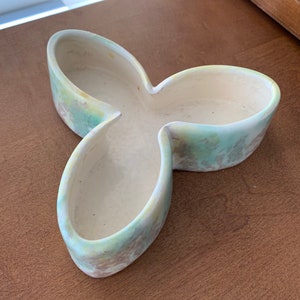 Könnte beinhalten: Eine dreilappige Keramikschale mit grüner und gelber Glasur. Die Schale hat drei Abschnitte, jeder mit einer abgerundeten Form.