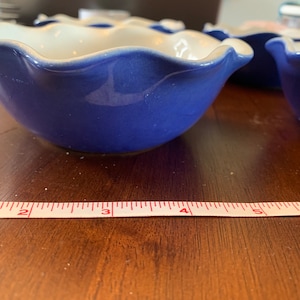 Peut inclure: Quatre bols en céramique bleu et blanc avec des bords festonnés. Les bols sont disposés en rangée sur une surface en bois. Un ruban à mesurer blanc avec des marques rouges est visible au premier plan.