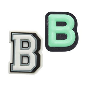 May include: Two letter "B" charms. One is white with black and gray accents, the other is a glowing green with a black border. These charms are likely for shoes or accessories.