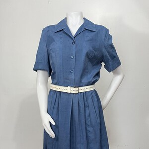 May include: A blue short-sleeved dress featuring a collared neckline, a button-down front with three visible buttons, and a subtle diamond-patterned texture. The dress is cinched at the waist with a white perforated belt featuring a silver buckle.