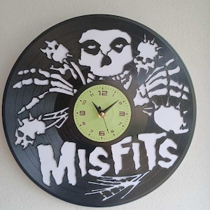 May include: A black vinyl record clock featuring a white skeleton with the band name "Misfits" printed in white. The clock face is a light green color with black numbers.