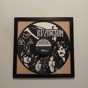 May include: Framed Led Zeppelin vinyl record art. The black record features the band's name and faces of the band members. The record is set against a tan background and framed in a black frame. The record label is visible.