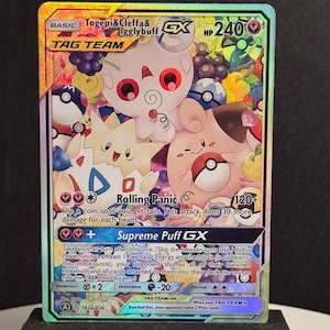May include: A holographic Pokémon trading card featuring Togepi, Cleffa, and Igglybuff. The card has a colorful background with the text "TAG TEAM" and "GX". The card's HP is 240, and it has the "Rolling Panic" and "Supreme Puff GX" attacks.