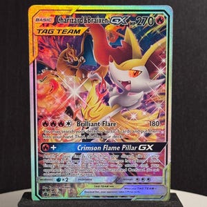 May include: A Charizard & Braixen GX Tag Team trading card. The card features a vibrant illustration of the two characters with a fiery background. The card has a HP of 270 and includes the text "Brilliant Flare" and "Crimson Flame Pillar GX".