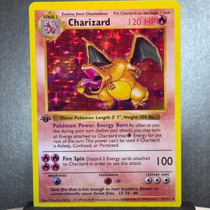 Puede incluir: Carta Pokémon Charizard, con un dragón naranja con alas extendidas. Borde amarillo, texto que detalla habilidades, incluyendo "Fire Spin". La carta mide 170 cm de largo y pesa 90,7 kg. Carta de nivel 2.