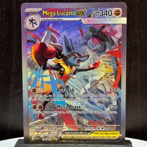 Puede incluir: Una carta Pokémon Mega Lucario EX, con un personaje Lucario azul y amarillo con detalles en rojo. La carta muestra el texto "Mega Lucario EX" y "Aura Jab 130". La carta se exhibe en un soporte negro.