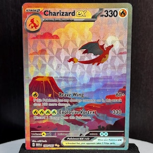 May include: A holographic Charizard EX Pokémon card, displayed on a black stand. The card features a red and orange dragon with a volcano and text that reads "Brave Wing" and "Explosive Vortex". The card is labeled "199/165".