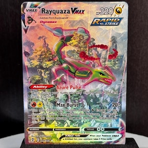 May include: A Rayquaza VMAX Pokémon card with a green and pink dragon illustration. The card features the text "Rayquaza VMAX", "Rapid Strike", and "Azure Pulse". The card is displayed on a black stand.