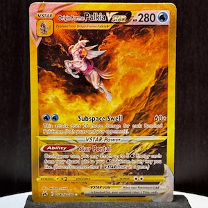 May include: A gold-bordered Origin Forme Palkia VSTAR Pokémon card. The card features a white and pink creature with wings against a fiery orange and yellow background. Text includes "Subspace Swell" and "Star Portal" abilities, along with the HP of 280.