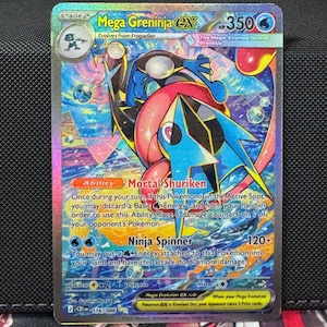 以下が含まれることがあります： ホログラフィックのメガゲニンジャEXポケモンカード。カードには、青と赤のゲニンジャのキャラクターが描かれており、「メガゲニンジャEX」と「Mortal Shuriken」と「Ninja Spinner」の能力が記載されています。カードにはステージ2の指定があります。