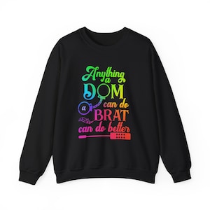 Può includere: Felpa nera con una grafica arcobaleno che dice "Anything a Dom can do a Brat can do better". La grafica include una frusta, manette e una piuma.