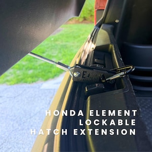 May include: A black metal Honda Element lockable hatch extension featuring a silver threaded rod and a black carabiner. The device is attached to the vehicle's rear hatch latch mechanism. The text Honda Element Lockable Hatch Extension is visible.