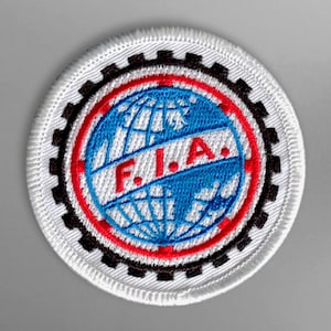 Peut inclure: Écusson brodé blanc avec une bordure noire en forme de roue dentée, un anneau rouge et un globe bleu avec les lettres "F.I.A." en rouge.