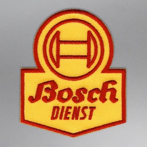 Peut inclure: Écusson brodé avec un fond jaune et une bordure rouge. Le patch présente le logo Bosch en haut et les mots "Bosch DIENST" en script rouge. Le patch a une forme rectangulaire avec un dessus circulaire.