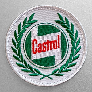 Puede incluir: Parche blanco bordado con un logotipo verde y blanco de la palabra "Castrol" en letras rojas, rodeado de una corona de laurel verde.