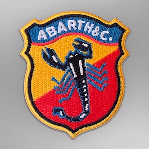 Könnte beinhalten: Ein gestickter Aufnäher in Gelb, Rot und Blau mit dem Text "ABARTH & C." und einem schwarzen Skorpion mit weißen Markierungen.
