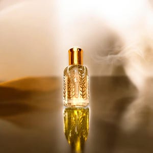 May include: A clear glass bottle with a gold cap and intricate gold designs. The bottle is filled with a light yellow liquid and is sitting on a reflective surface.