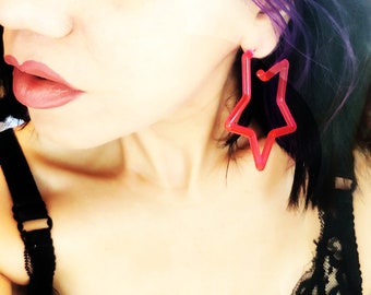 May include: A woman with purple and black hair wearing a black lace bra and large red star-shaped earrings.