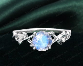 Op de afbeelding: Een zilveren ring met een ronde maansteen en twee kleine diamanten in een rankontwerp.