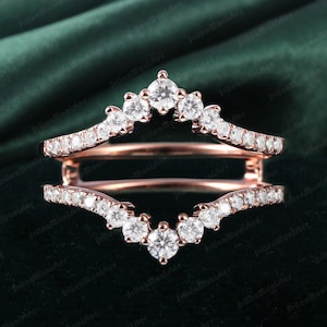 Op de afbeelding: Een ringversterker van roségoud met een gebogen ontwerp en een rij kleine diamanten aan elke kant. De versterker heeft een kroonvormige bovenkant met grotere diamanten.
